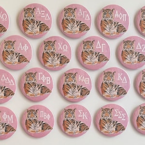 Op de afbeelding: Vierentwintig ronde roze knoppen met een tijgerillustratie en witte Griekse letters. De letters staan voor verschillende sororities.
