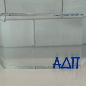 May include: A clear acrylic block with the letters "AΔΠ" in blue lettering.