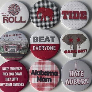 Könnte beinhalten: Eine Sammlung von neun runden Ansteckbuttons mit verschiedenen Motiven in Rot, Weiß und Grau. Die Buttons zeigen Texte wie This Is How We Roll, Tide, Beat Everyone, Game Day, Alabama Mom sowie Sätze, die eine Rivalität ausdrücken.