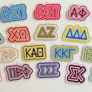May include: A collection of 15 colorful sorority Greek letter charms. The charms are made of acrylic and feature different sorority names, including Alpha Delta Pi, Chi Omega, Delta Zeta, Kappa Alpha Theta, and Sigma Kappa.