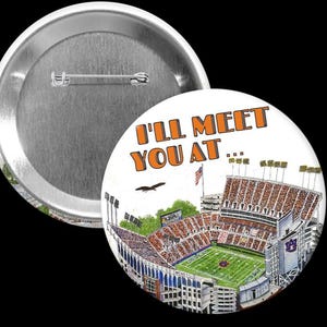 May include: A round button with a stadium illustration and the text "I'll MEET YOU AT...". The stadium has a green field, orange seating, and the Auburn University logo. The button is white with orange and green accents.
