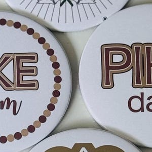 May include: White round buttons with the words "PIKE" in brown and tan lettering. One button says "mom" in a script font, and another says "dad". A third button is partially visible.