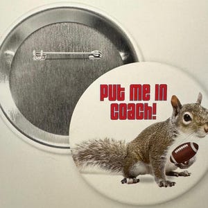 May include: A white button featuring a grey squirrel holding a football. The text "Put me in coach!" is printed in red.