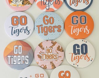 May include: A collection of round buttons with the text "Go Tigers" in various designs. Some buttons feature a tiger illustration, while others have patterns or star accents. The color palette includes orange, blue, and pink.