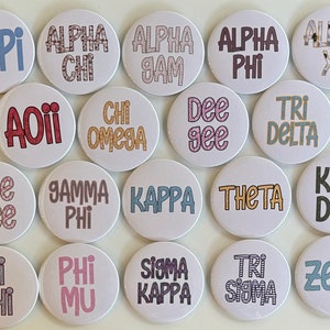 Puede incluir: Una colección de 16 botones redondos con varios nombres y abreviaturas de hermandades impresos en ellos. Los botones son blancos con texto y diseños coloridos. Los nombres de las hermandades incluyen: ADPI, Alpha Chi, Alpha Gam, Alpha Phi, Alpha Xi, AOTI, Chi Omega, Dee Gee, Tri Delta, Dee Zee, Gamma Phi, Kappa, Theta, Kay Dee, Pi Phi, Phi Mu, Sigma Kappa, Tri Sigma y Zeta.
