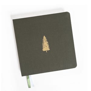 May include: A dark green notebook with a gold-colored tree design in the center. The notebook has a ribbon bookmark with green and white stripes. The cover has a textured appearance.