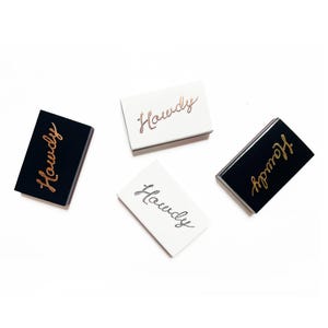May include: Four matchboxes with the word "Howdy" written on them in gold script. Two matchboxes are black with white lettering and two are white with gold lettering.