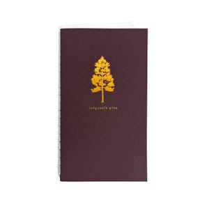 May include: A rectangular notebook with a dark maroon cover featuring a gold foil-stamped silhouette of a tree and the text lodgepole pine printed in gold below the tree. The notebook has a white stitched spine visible on the left side.