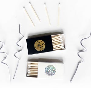 May include: Two boxes of matches with a disco ball design. One box is black with a gold disco ball and the other is white with a silver disco ball.