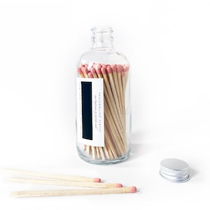 May include: A glass bottle filled with wooden matches with pink tips. The bottle has a label that reads "for special & everyday use studio portmanteau".