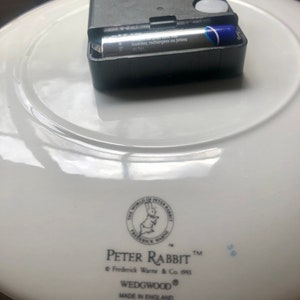 The reverse of the plate includes a small black clock mechanism which takes an AA battery. The World of Peter Rabbit logo and Peter Rabbit and Wedgewood name can be seen along with Made in England