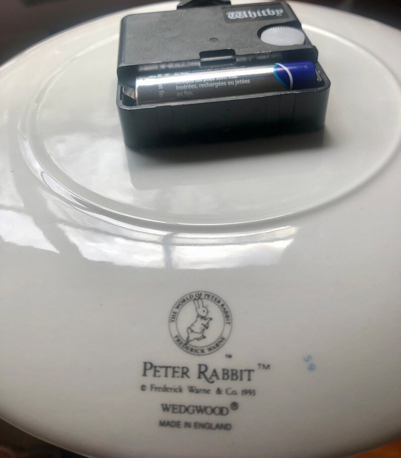 The reverse of the plate includes a small black clock mechanism which takes an AA battery. The World of Peter Rabbit logo and Peter Rabbit and Wedgewood name can be seen along with Made in England