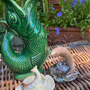 May include: A large green ceramic fish-shaped pitcher with a textured scale pattern, accompanied by two smaller iridescent ceramic fish figurines, one of which is mounted on a base with the text LANDS END printed on the side.