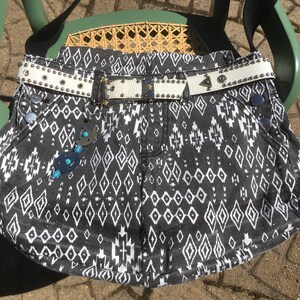 May include: A black and white patterned denim bag with a white studded belt. The bag has a geometric design and is decorated with turquoise and silver embellishments.