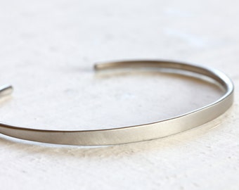 May include: A simple silver bangle bracelet with a brushed finish.