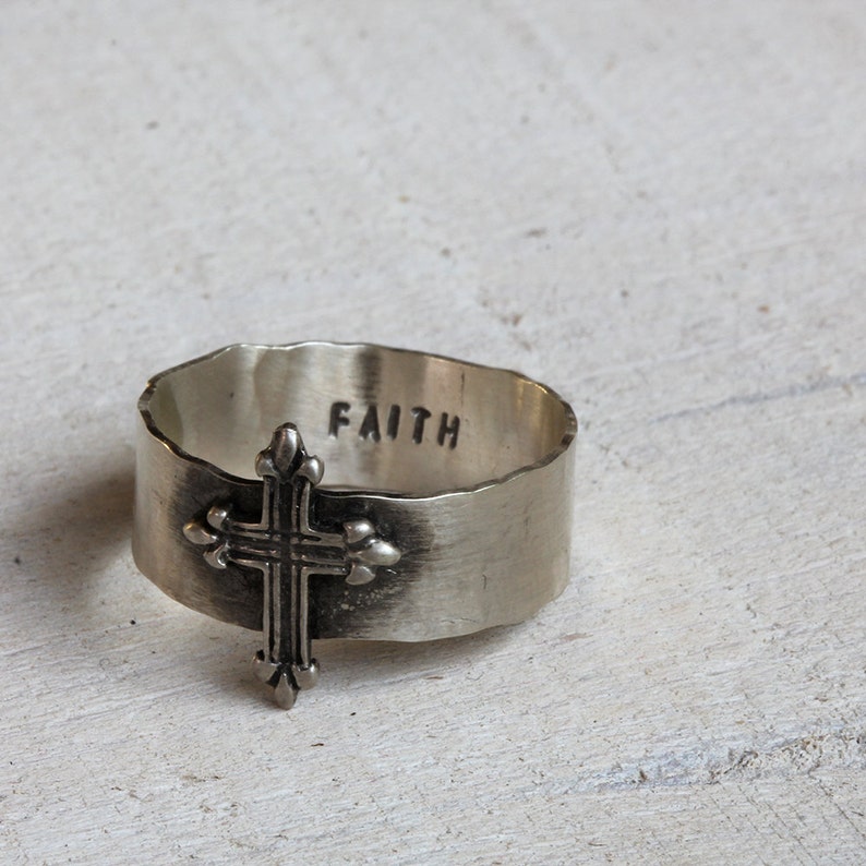 May include: A silver ring with a cross design and the word "FAITH" engraved on the band.