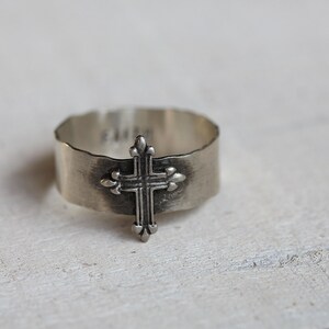 May include: A silver ring with a cross design. The ring is textured and has a hammered finish.