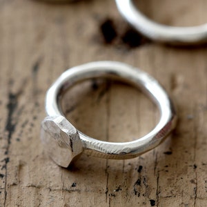 May include: A silver ring with a hammered, octagonal band. The ring is made of metal and has a simple, modern design.