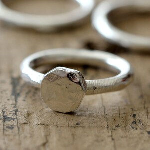 May include: A silver ring with a hammered, octagonal-shaped band and a textured, hammered, octagonal-shaped top.
