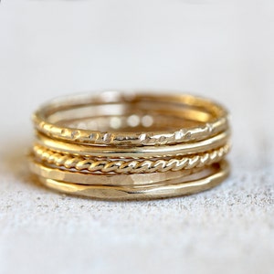 May include: A set of five gold stacking rings. The rings are all different styles, including a hammered ring, a rope ring, and a plain band.