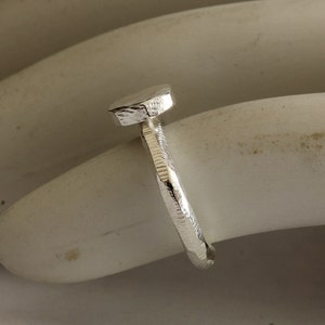 May include: A silver ring with a textured, rounded top. The ring is made of a hammered metal and has a unique, organic shape.
