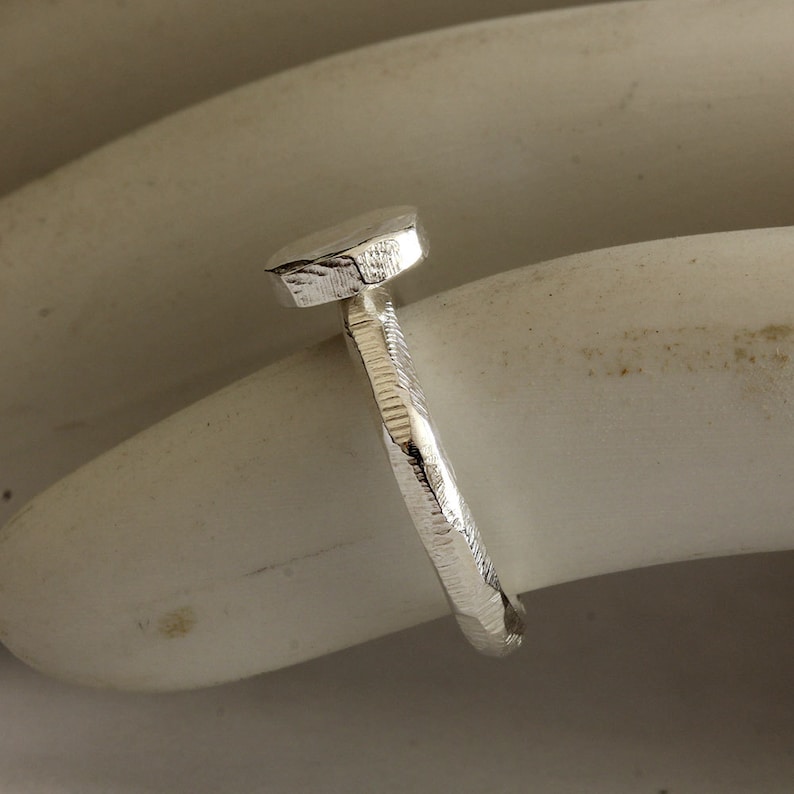 May include: A silver ring with a textured, rounded top. The ring is made of a hammered metal and has a unique, organic shape.