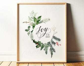 May include: A framed print featuring a watercolor wreath of green holly, pine, and eucalyptus leaves surrounding the black calligraphic text Joy to the World! set against a white background within a light wood frame.