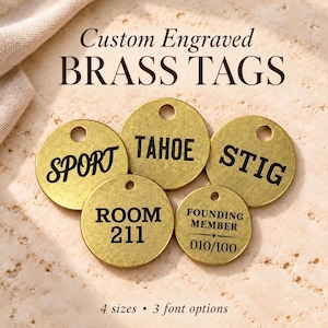 Può includere: Cinque etichette circolari in ottone con testo inciso in nero. Le etichette riportano le parole SPORT, TAHOE, STIG, ROOM 211 e FOUNDING MEMBER 010/100. Ogni etichetta ha un piccolo foro in alto. Appare il testo Custom Engraved BRASS TAGS e 4 sizes 3 font options.
