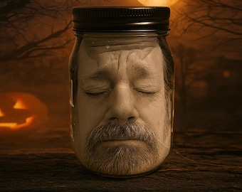 May include: A clear glass jar with a black lid containing a realistic, sepia-toned image of a man's face with closed eyes and a mustache. The face appears to be pressed against the interior glass, creating a distorted, three-dimensional effect.