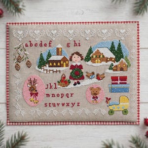 Puede incluir: Un muestrario de punto de cruz rectangular sobre tela beige con borde de cuadros rojos. Incluye el alfabeto en minúsculas rojas, una figura central con una corona, cabañas invernales, pinos, un reno, un oso, regalos y un cochecito amarillo.