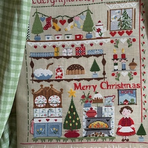 Puede incluir: Sampler navideño de punto de cruz con elementos festivos. Presenta un árbol de Navidad, calcetines, regalos y el texto "Merry Christmas" y "Waiting for christmas, one stitch at a time". El diseño incluye un borde decorativo y una tela de cuadros verdes y blancos.