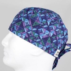 May include: A blue, green, and purple patterned surgical scrub hat with a tie at the back. The hat has a small white label with the text "Scrubs" on it.