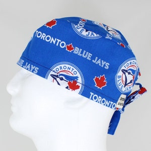 May include: Blue and white surgical scrub hat with a repeating pattern of the Toronto Blue Jays logo. The hat has a tie at the back.