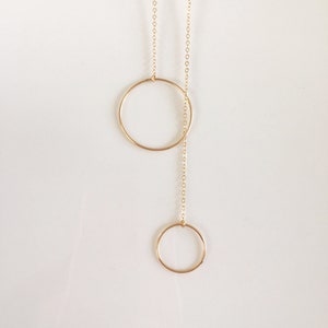 May include: A gold chain necklace with two circular pendants. The larger circle is at the top of the chain and the smaller circle is at the bottom.