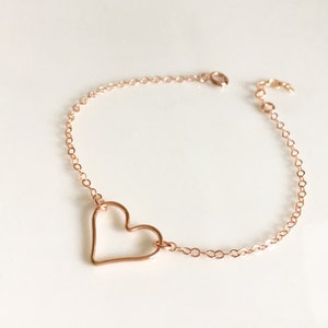 May include: A delicate rose gold chain bracelet with a simple open heart charm.