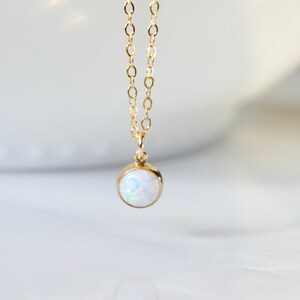 May include: A delicate gold chain necklace with a small, round opal pendant. The opal is white with a hint of iridescent color.