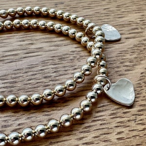 May include: Two gold beaded bracelets with heart-shaped charms. The charms are silver and have a hammered texture.