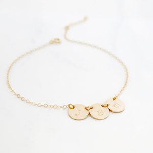 May include: A gold chain bracelet with three small round charms, each engraved with a letter: J, B, and M.