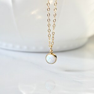 May include: A delicate gold chain necklace with a small, round white opal pendant.