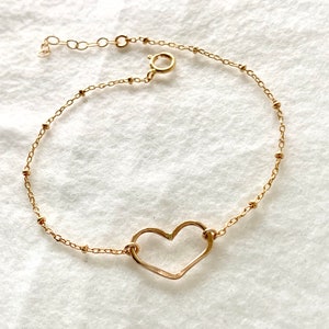 May include: A gold chain bracelet with a delicate open heart charm. The chain is made of small, round beads.