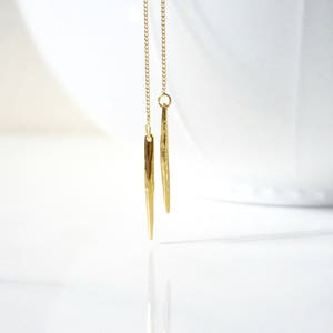 May include: A pair of gold dangle earrings with long, thin, pointed drops.