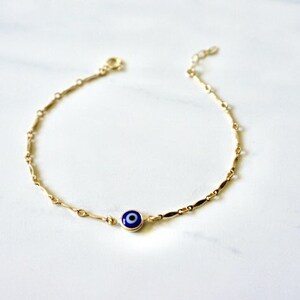 May include: A gold chain anklet with a blue evil eye charm.
