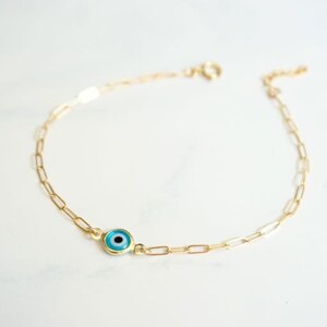 May include: A gold chain bracelet with a blue evil eye charm. The chain is made of small, linked circles.