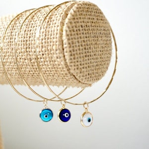 May include: Three gold bangle bracelets with evil eye charms. The charms are blue, dark blue, and white.