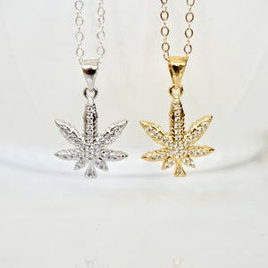May include: Two silver and gold necklaces with a marijuana leaf pendant encrusted with clear cubic zirconia stones.
