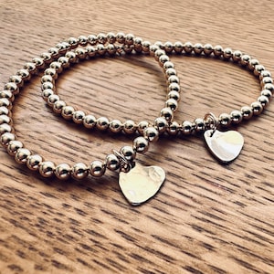 May include: Two gold beaded bracelets with heart-shaped charms. The charms are silver and have a hammered texture.