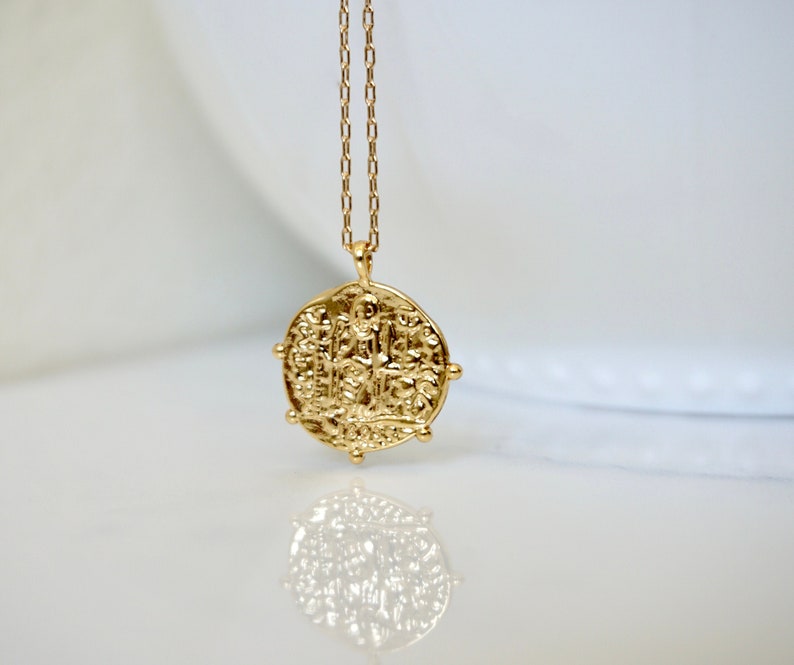 May include: Gold necklace with a large, round pendant featuring an intricate design. The pendant is reminiscent of an antique coin.