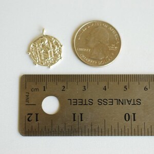 May include: Silver pendant charm with a detailed design of three figures, measuring approximately 1 inch in diameter. The pendant is shown next to a US quarter for size comparison.