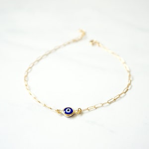 May include: A gold chain bracelet with a blue and white evil eye charm.