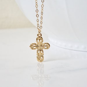 May include: A gold chain necklace with a delicate, ornate cross pendant. The cross is detailed with intricate floral designs.